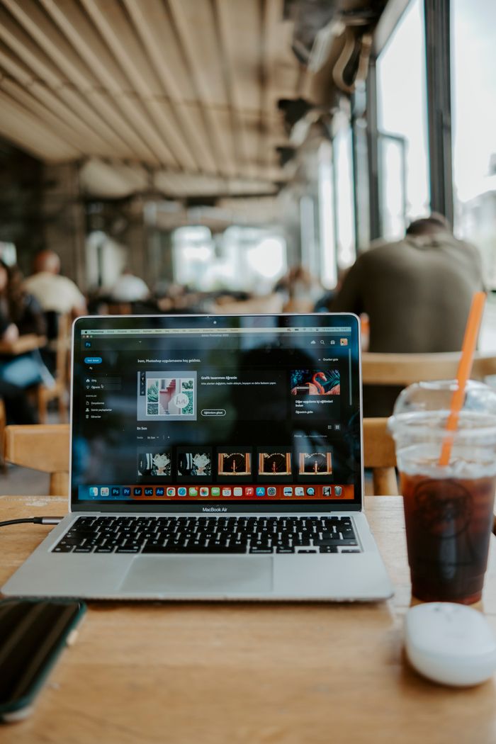 A laptop and iced coffee on a wooden table in a bustling cafe, ideal for remote work.